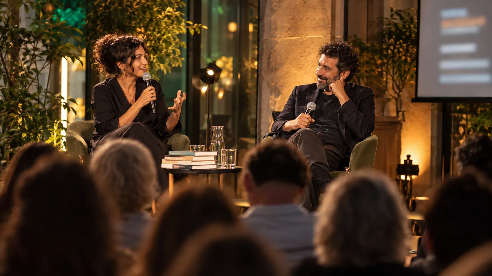 Two people speak into microphones during a literary evening before an audience.